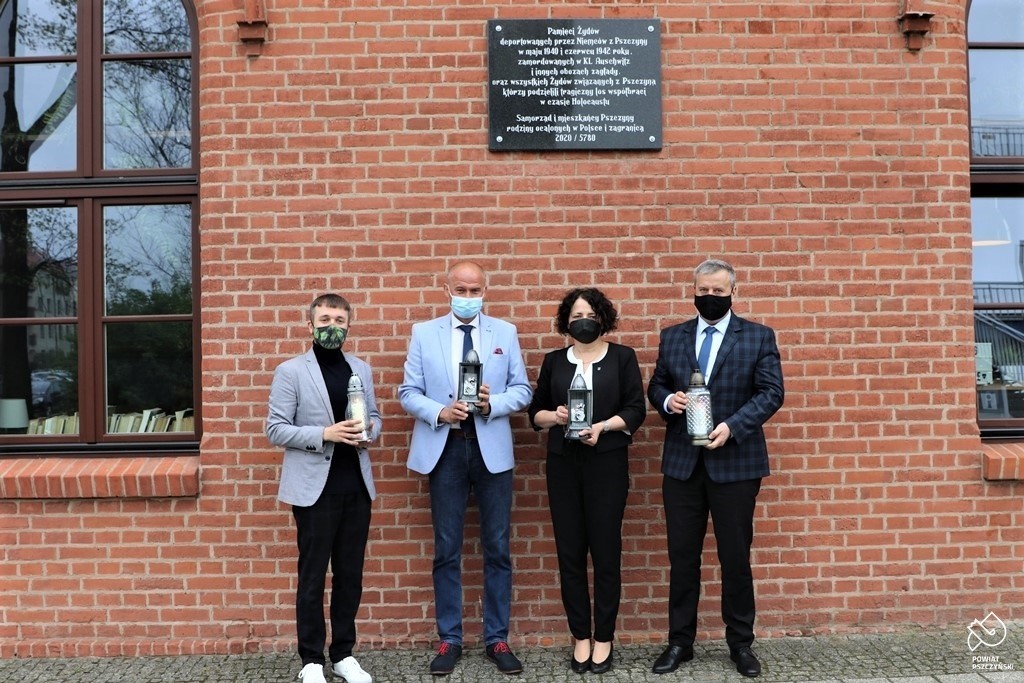 Starosta, zastępca burmistrza, sekretarz powiatu oraz Sławomir Pastuszka stojący przy pamiątkowej tablicy, w dłoniach trzymają zapalone znicze.