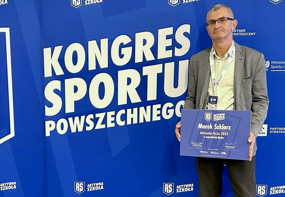 Mężczyzna na tle loga kongresu, trzyma w rękach tablicę z wyróżnieniem.