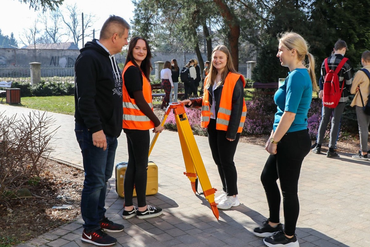 Dyrektor z uczennicami z klasy geodezyjnej, które pracują na sprzęcie.