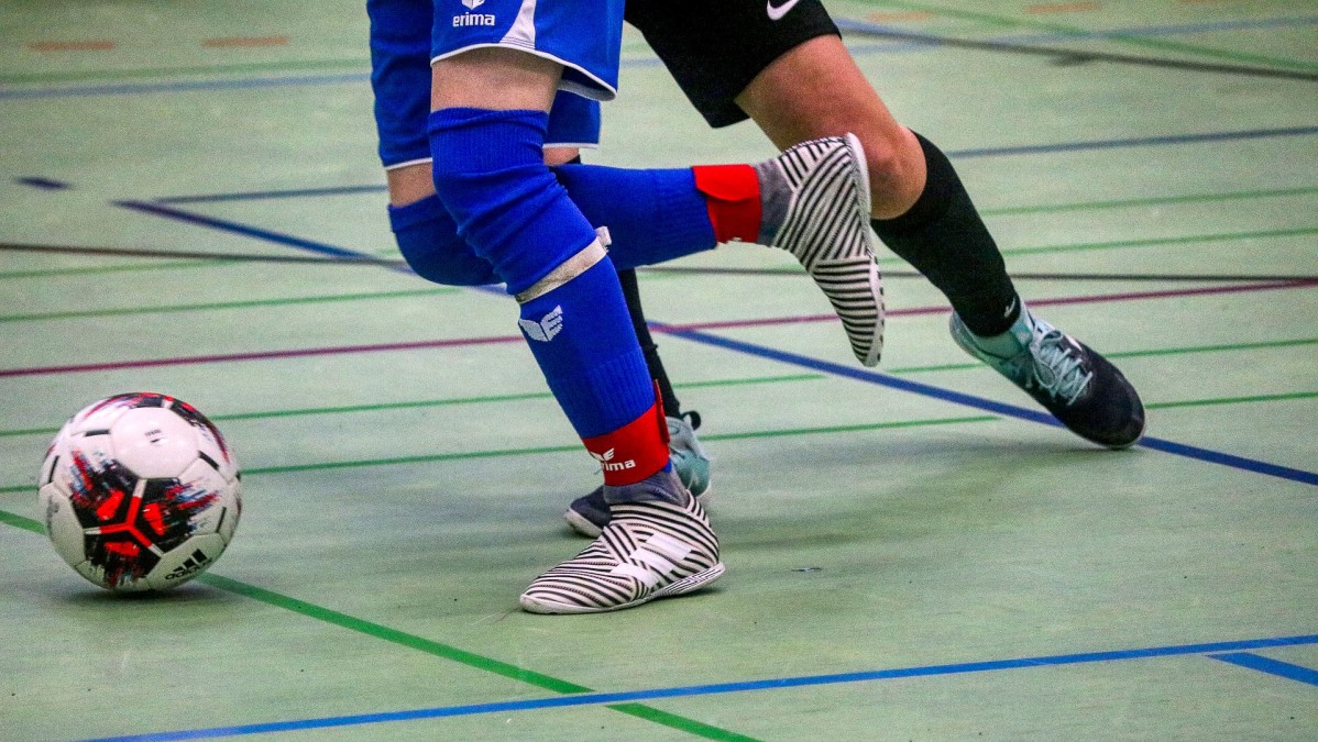 Zawodnicy biegnący za piłką na hali sportowej.