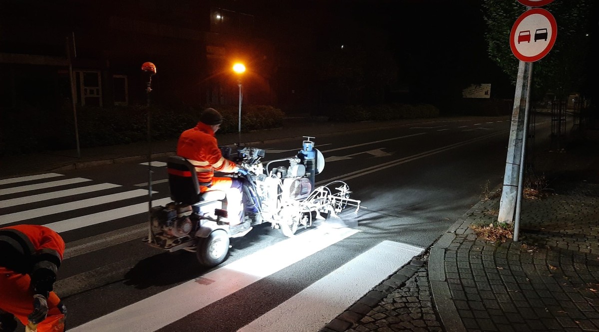 W nocy na ulicy pracownik ubrany w pomarańczowe ubranie maluje miały pasy na drodze