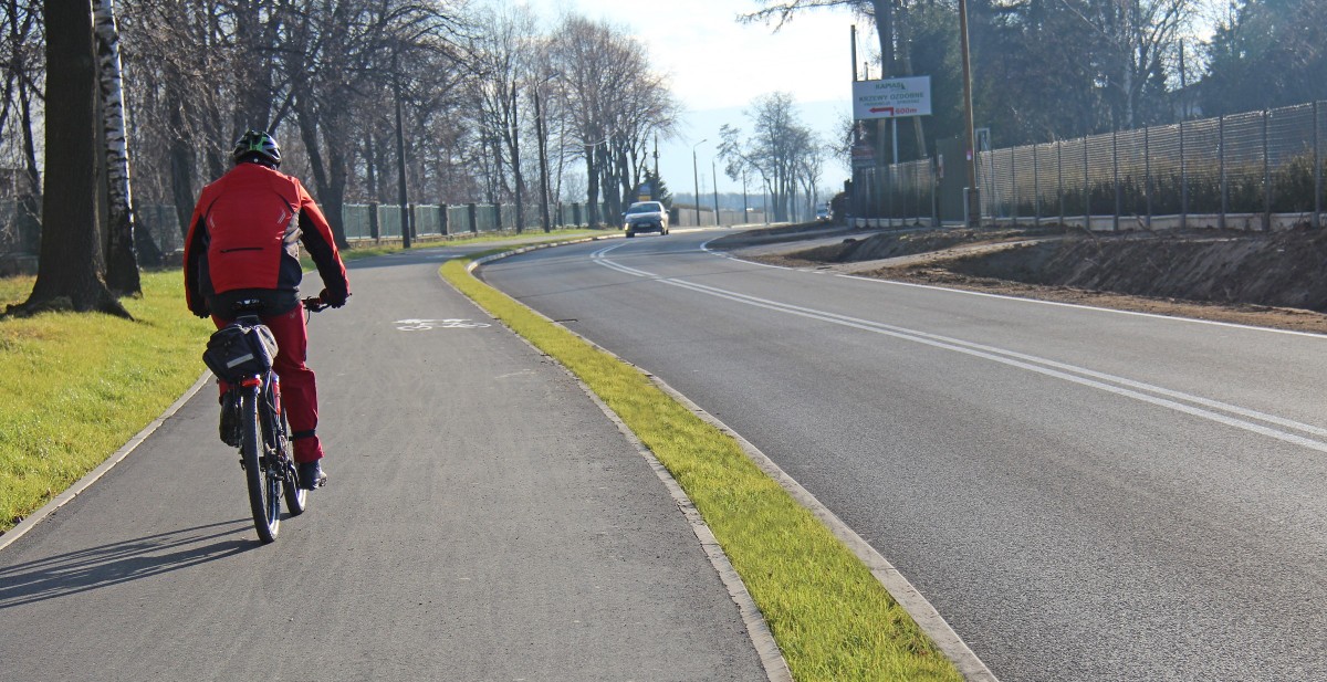 Droga rowerowa przy ul. Zdrojowej w Pszczynie, po której jedzie rowerzysta ubrany w czerwony strój i kask.