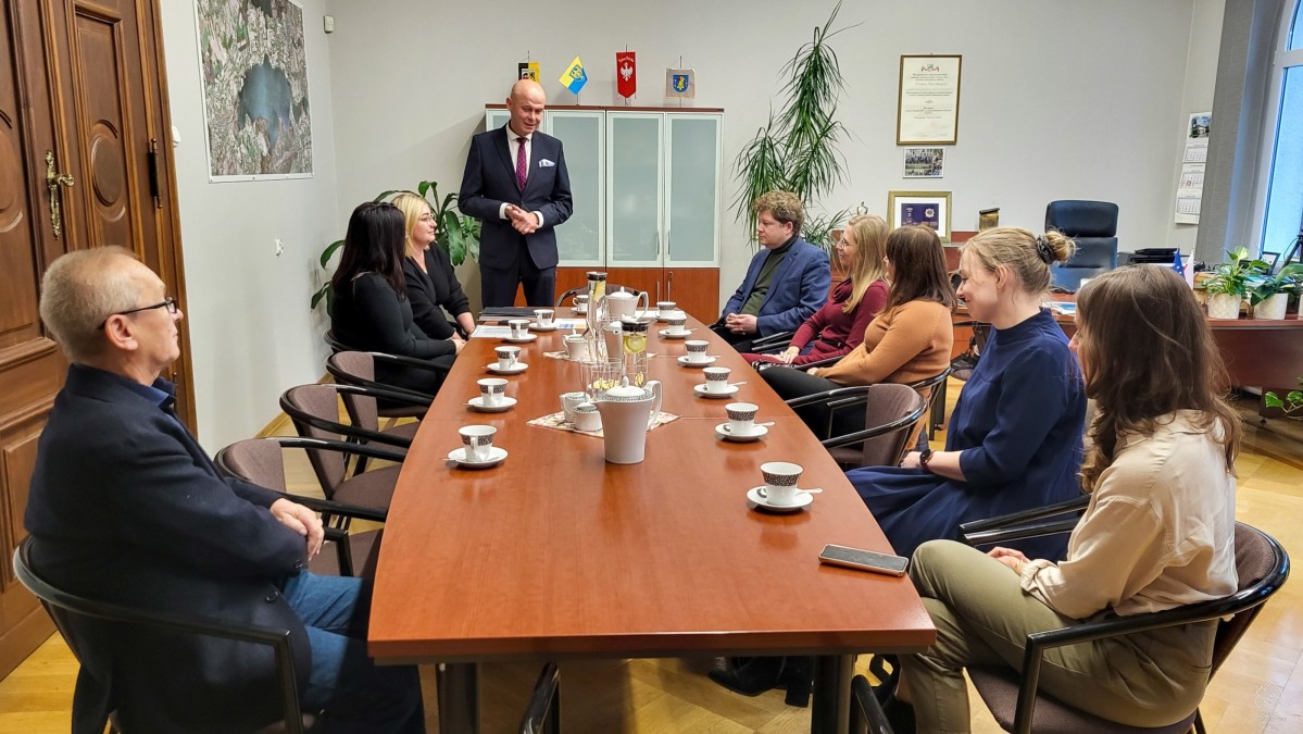 Przy stole siedzą adwokaci i radcy prawni oraz pracownicy starosta, przed nimi stoi sekretarz powiatu i przemawia w gabinecie starosty.