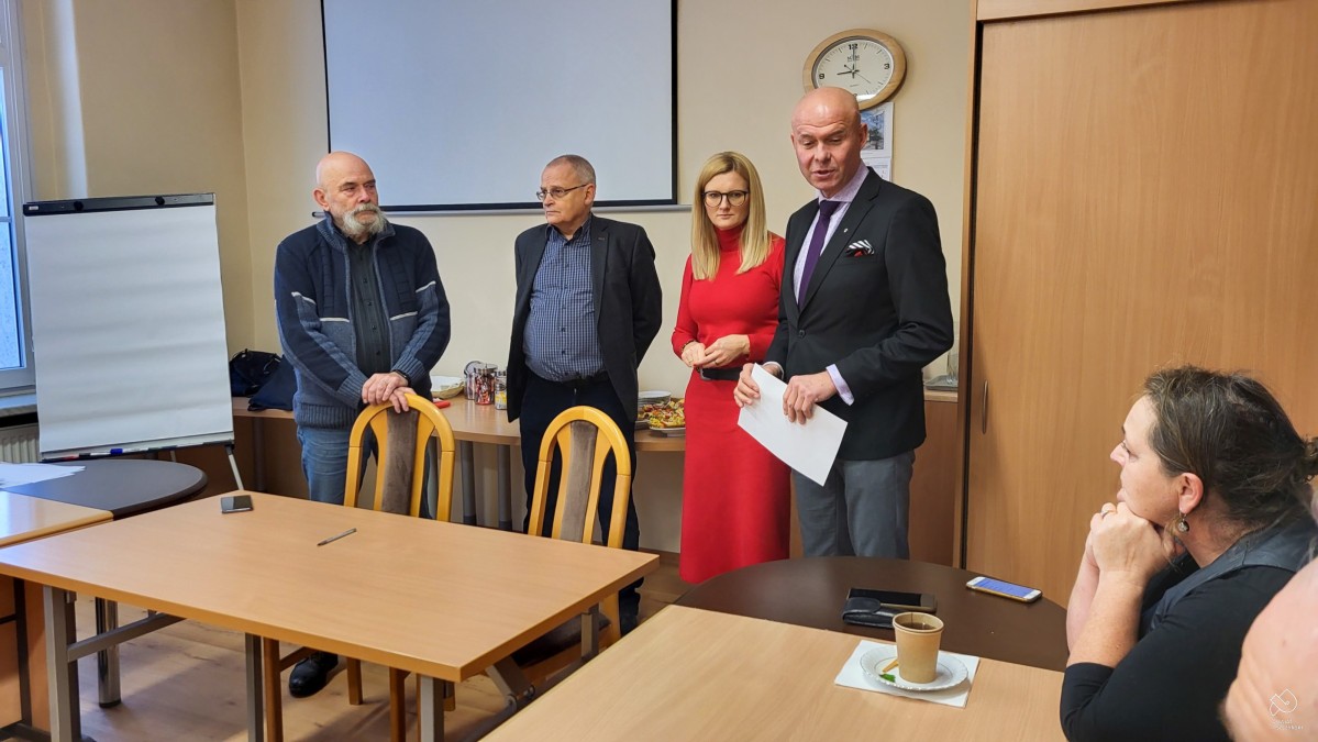 sekretarz powiatu, naczelniczka wydziału oraz szkoleniowcy stoją w pomieszczeniu, w którym przy stołach siedzą uczestnicy szkolenia