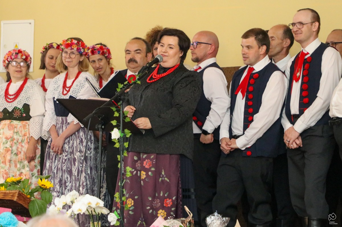 Członkowie i terapeuci zespołu folklorystycznego ubrani w regionalne stroje stoją na scenie.