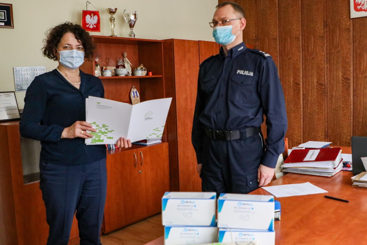 Starosta i koemndat policji stoją w pomieszczeniu, na stole stoją opakowania z jednorazowymi maseczkami.