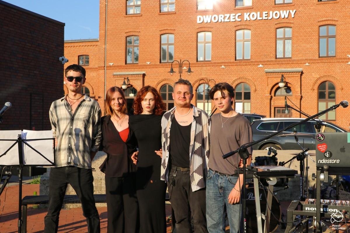 Grupa pięciu osób, które tworzą grupę Shelter przed budynkiem dworca.