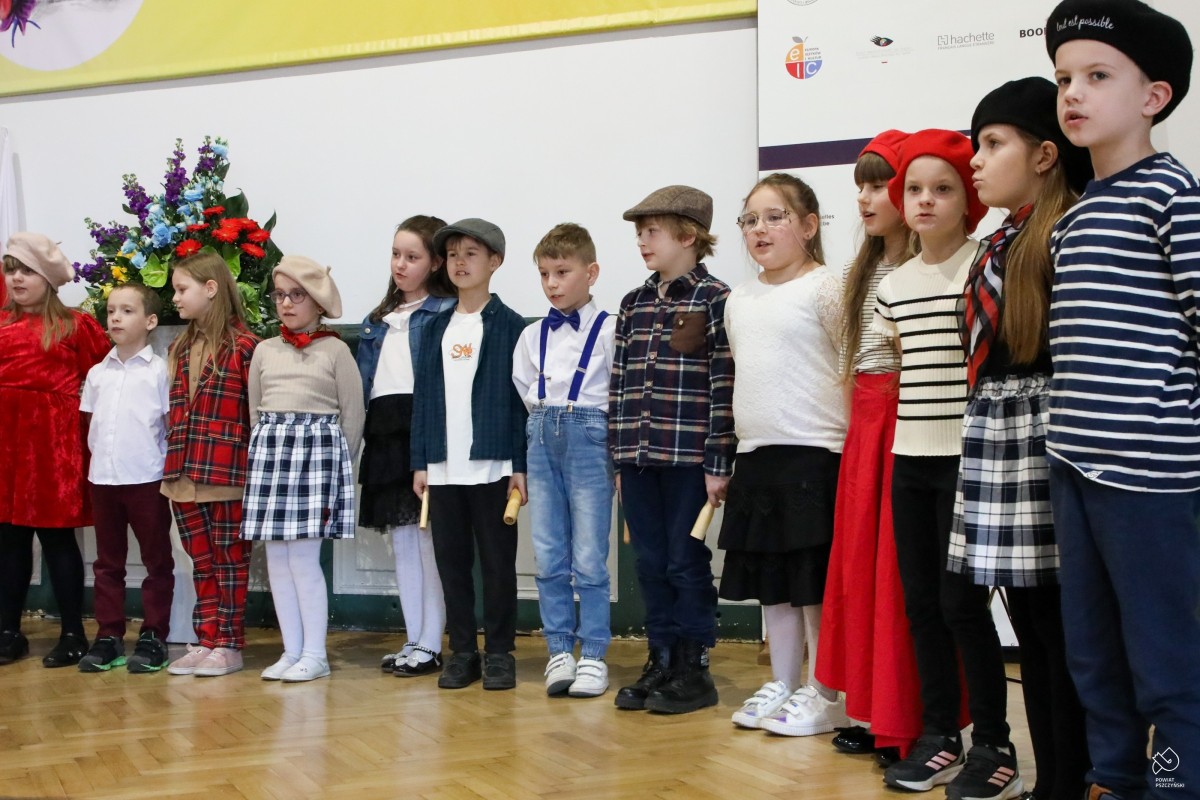 Uczniowie szkoły podstawowej ubrani w stroje charakterystyczne dla Francji stoją na scenie i śpiewają