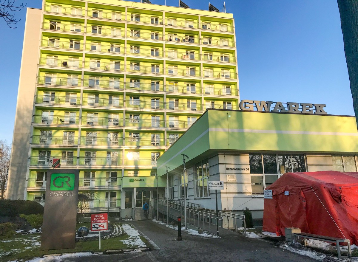 Wysoki szpitalny budynek z zieloną elewacją. Przed nim czerwony namiot.