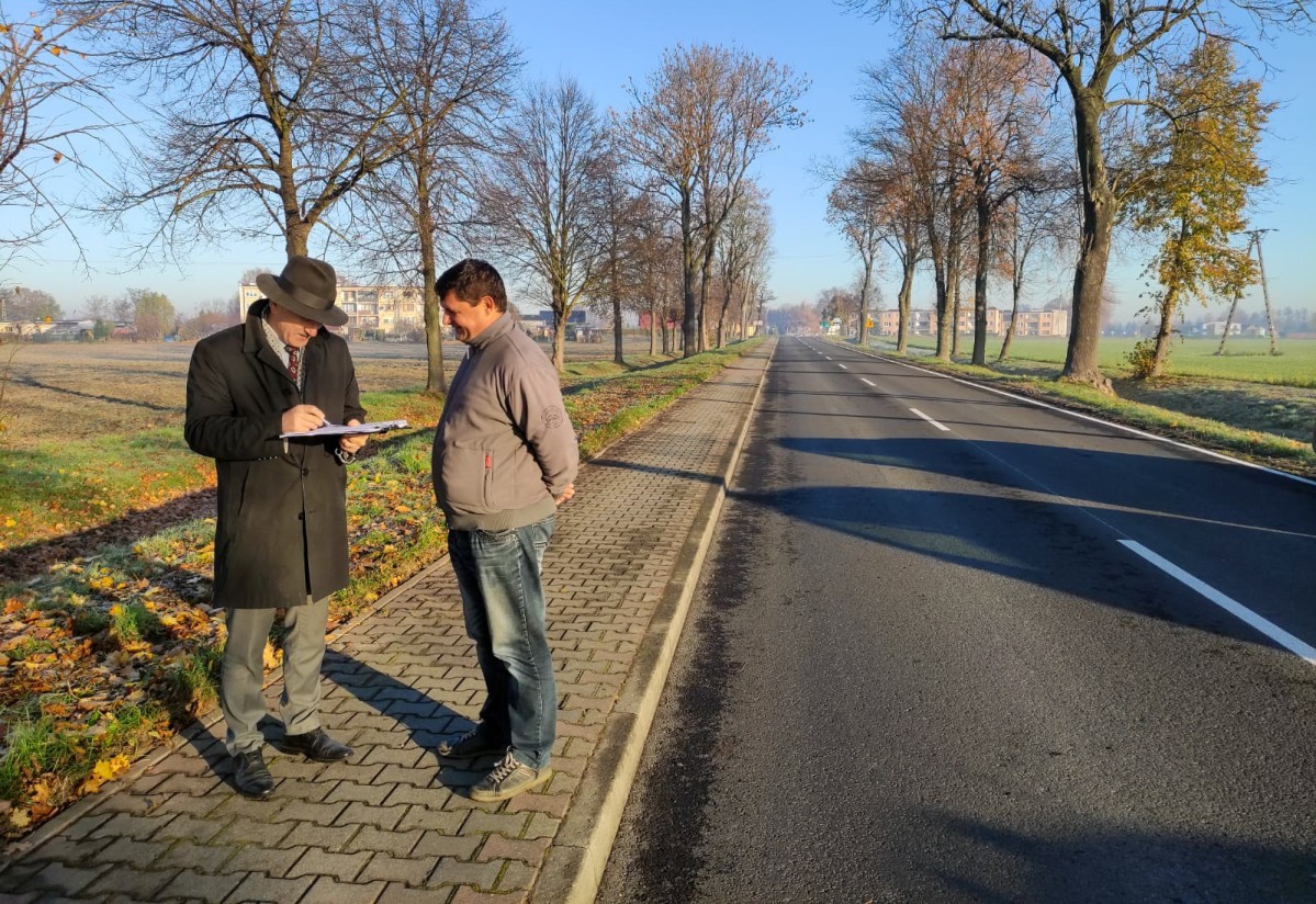 Grzegorz Nogły wraz z przedstawicielem firmy, która przeprowadziła naprawę. Stoją na chodniku i podpisują dokumenty.