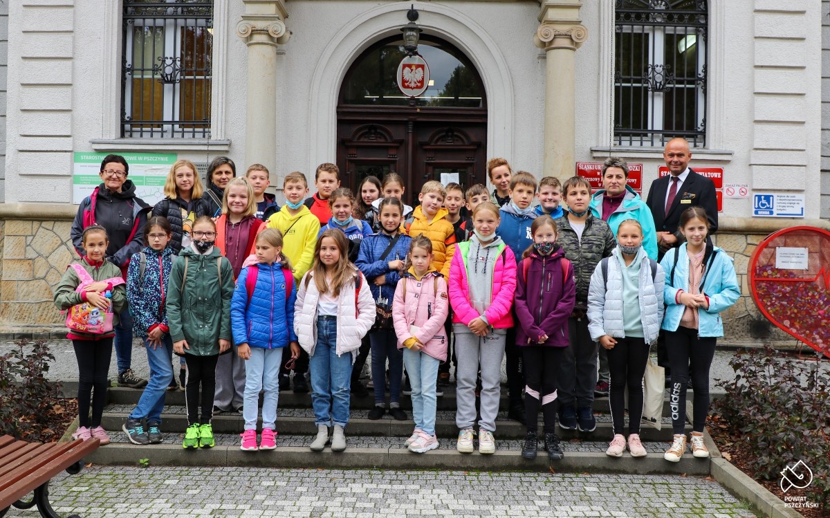 Dzieci wraz z opiekunkami i dyrektorem oraz sekretarzem powiatu pszczyńskiego przed budynkiem pszczyńskiego starostwa.