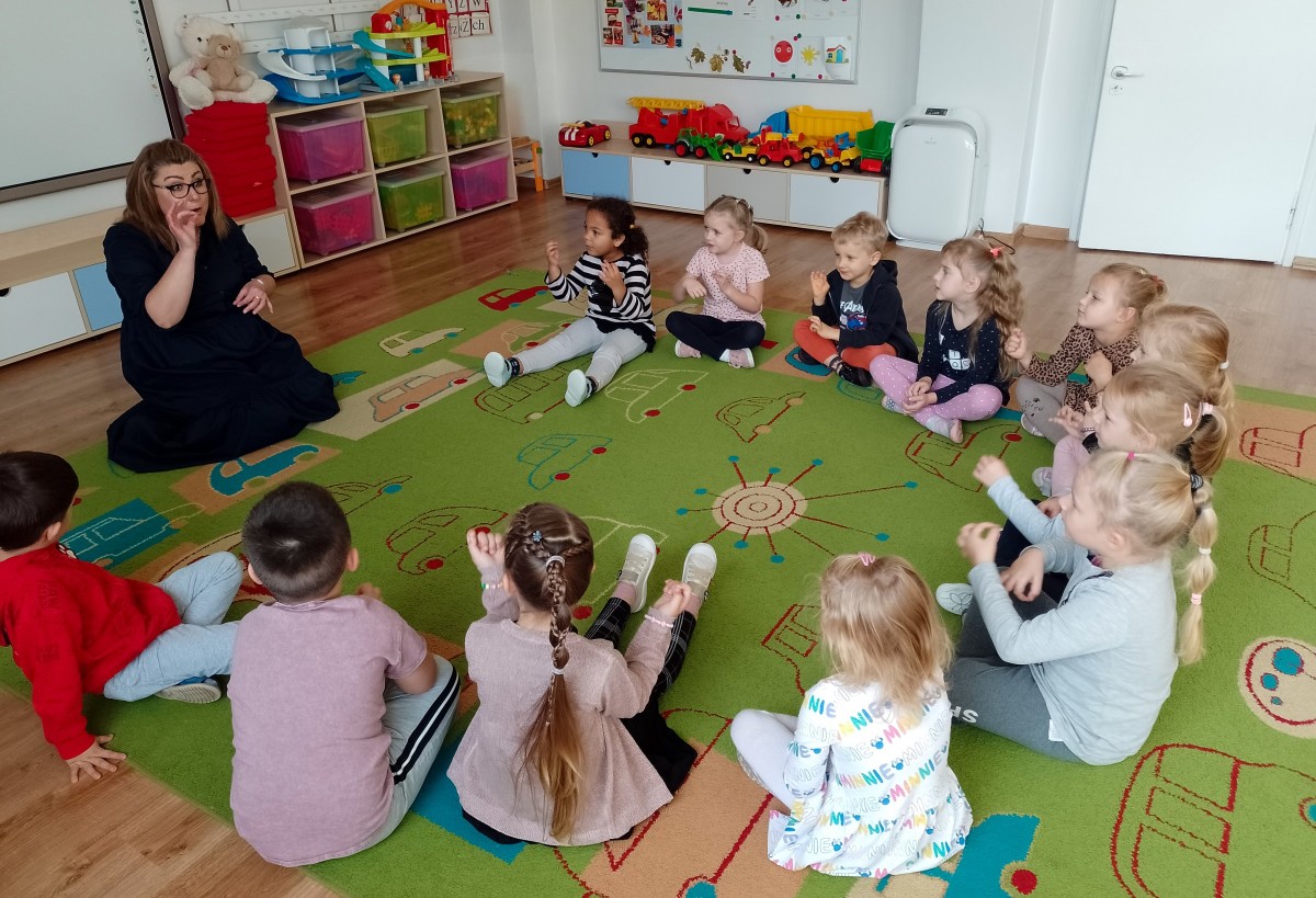 Dzieci siedzące na dywanie, migają palcami.