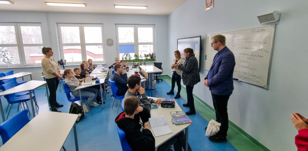 W klasie szkoły w Łące podczas lekcji uczniowie siedzą w ławkach, a przedstawiciele szkoły z Niemiec stoją