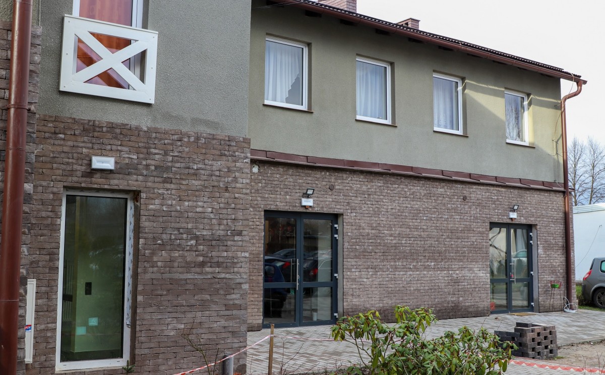 Wyremontowany budynek o szarej elewacji, dół w szarej cegle.