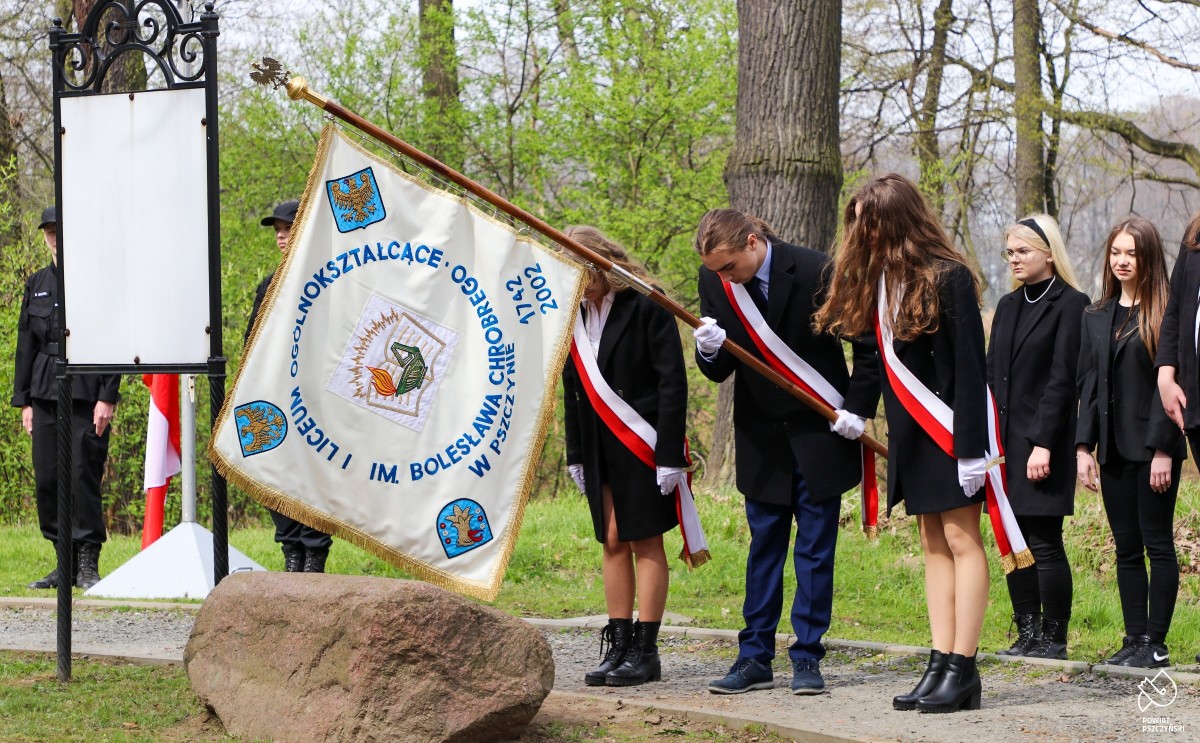 Uczniowie pochylający sztandar nad pomnikiem.