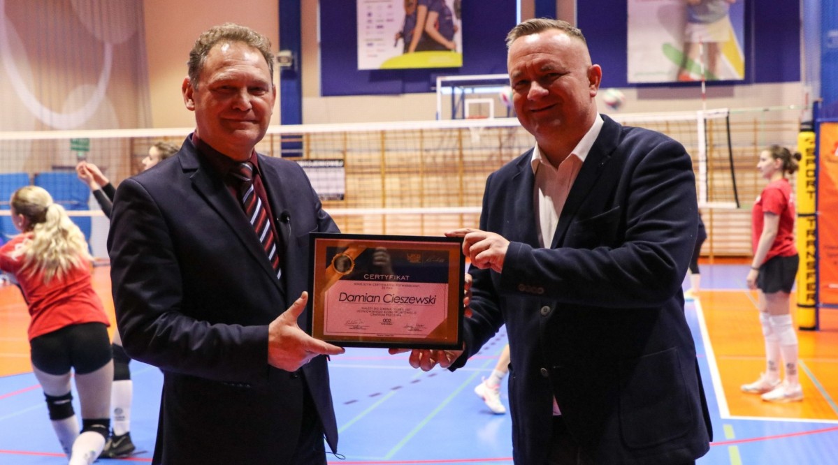 Wicestarosta Damian Cieszewski i dyrektor POSiR są na hali sportowej. Trzymają certyfikat.