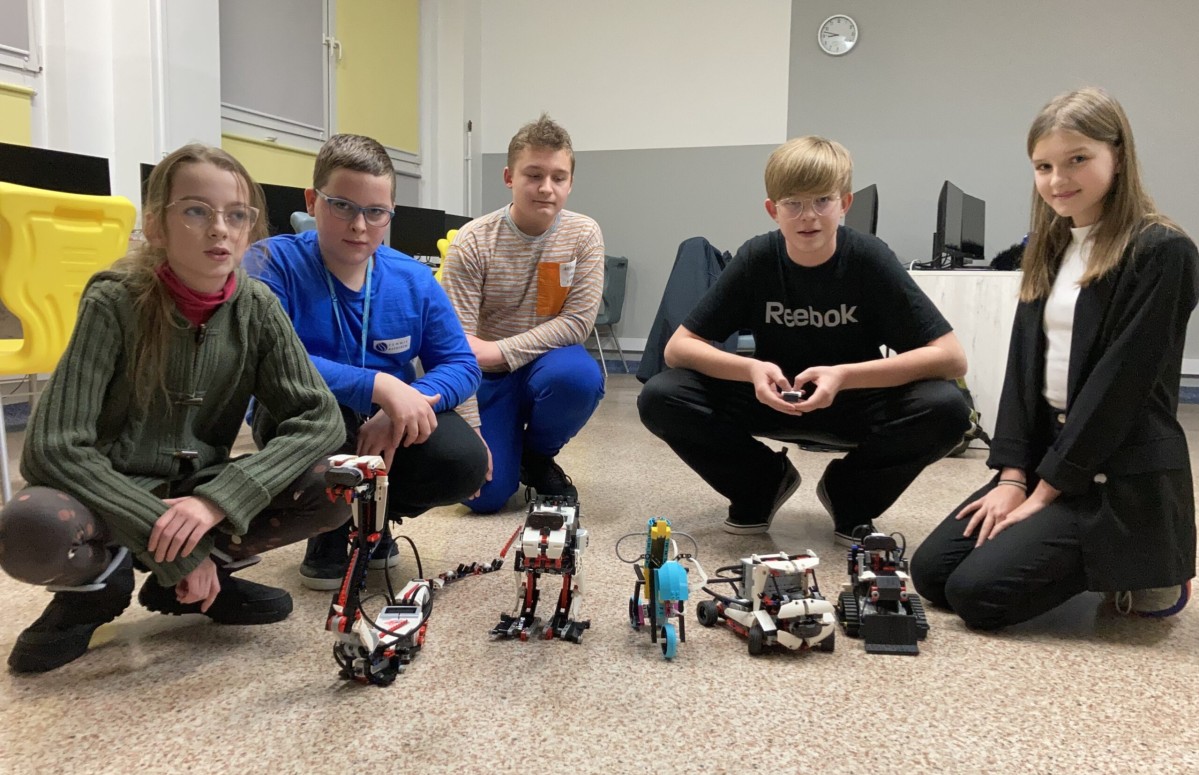 Dzieci uczestniczące w zajęciach lego robotyki kucają przy stworzonych przez siebie zestawach.