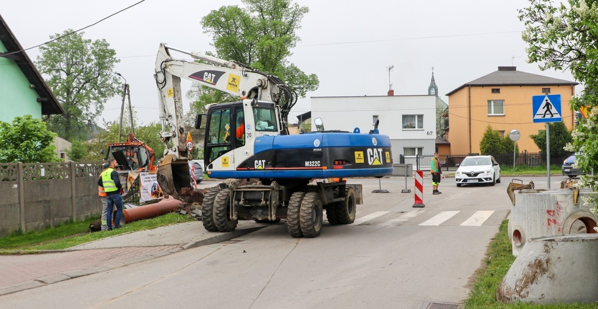Trwają roboty drogowe na ul. Studzienickiej w Piasku. Robotnicy drogowi i maszyny na drodze i poboczu, trwają wykopy.