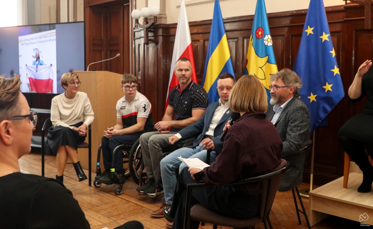 Uczestnicy panelu dyskusyjnego siedzą na krzesłach w sali sesyjnej.