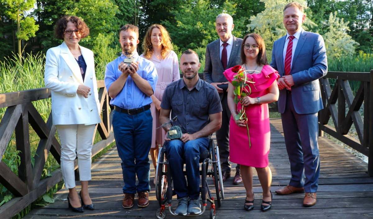 Laureaci wyróznienia uskrzydlony oraz władze powiatu stoją na drwnianym pomoście w skansenie.