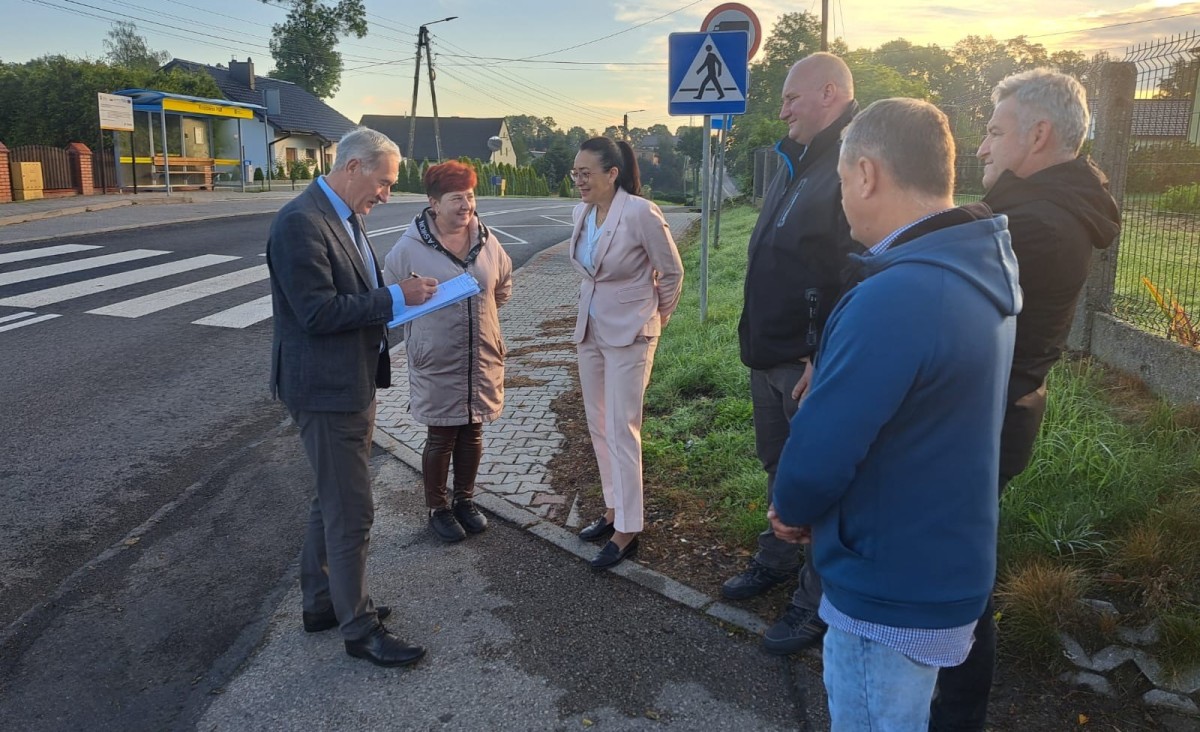 Przedstawiciele samorządów i sołtysi stoją przy wyremontowanej drodze i podpisują protokół odbioru robót.