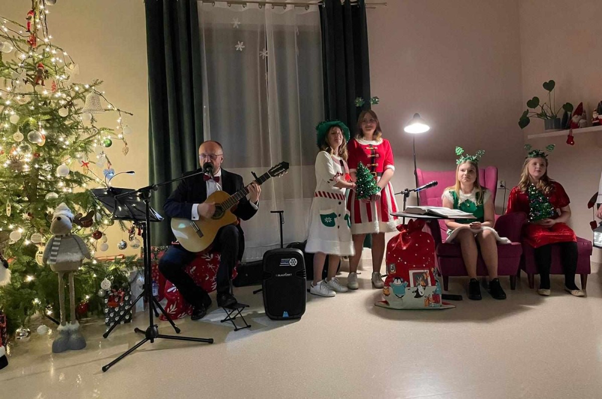 Występ jasełkowy podopiecznych CWDiR. N akrześle siedzi mężczyna grający na gitarze Dzieci stoją przebrane w świąteczne stroje.