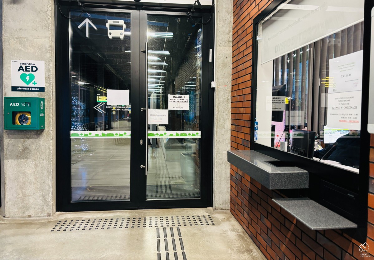 Wnętrzne budynku centrum przesiadkowego, na ścianie przy drzwiach wisi skrzynka z urządzeniem.