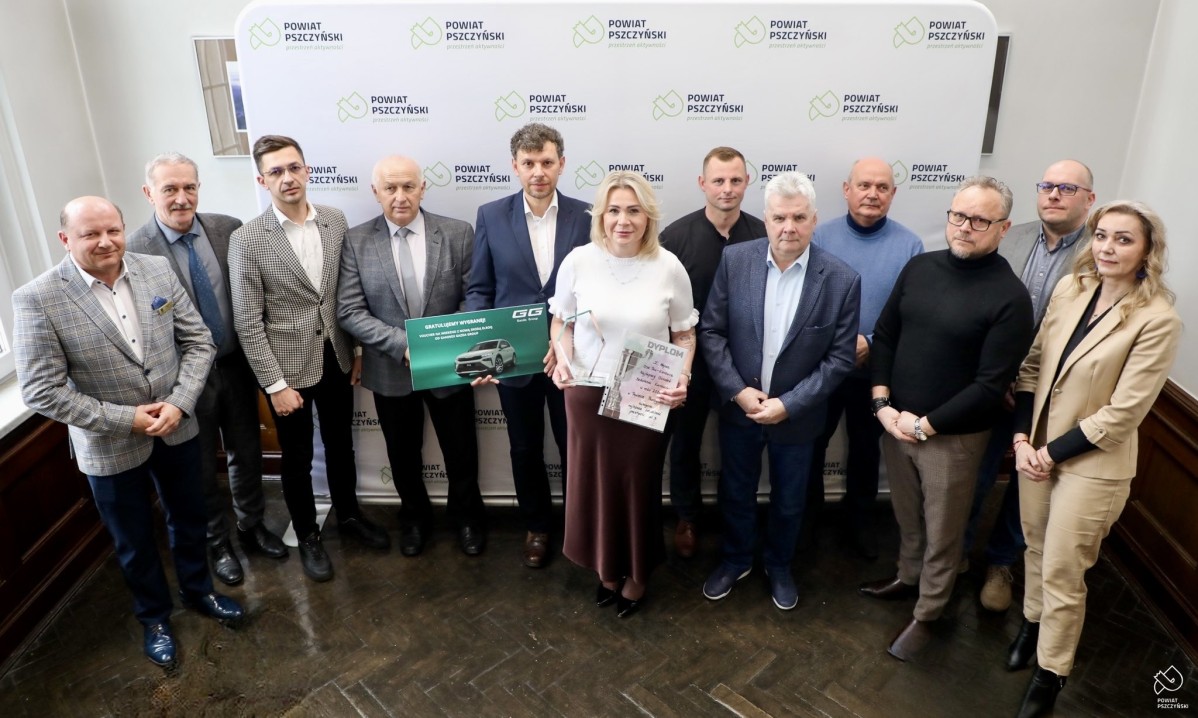 Wszyscy uczestnicy spotkania we wspólnym zdjęciu na tle ścianki z logiem Powiatu.
