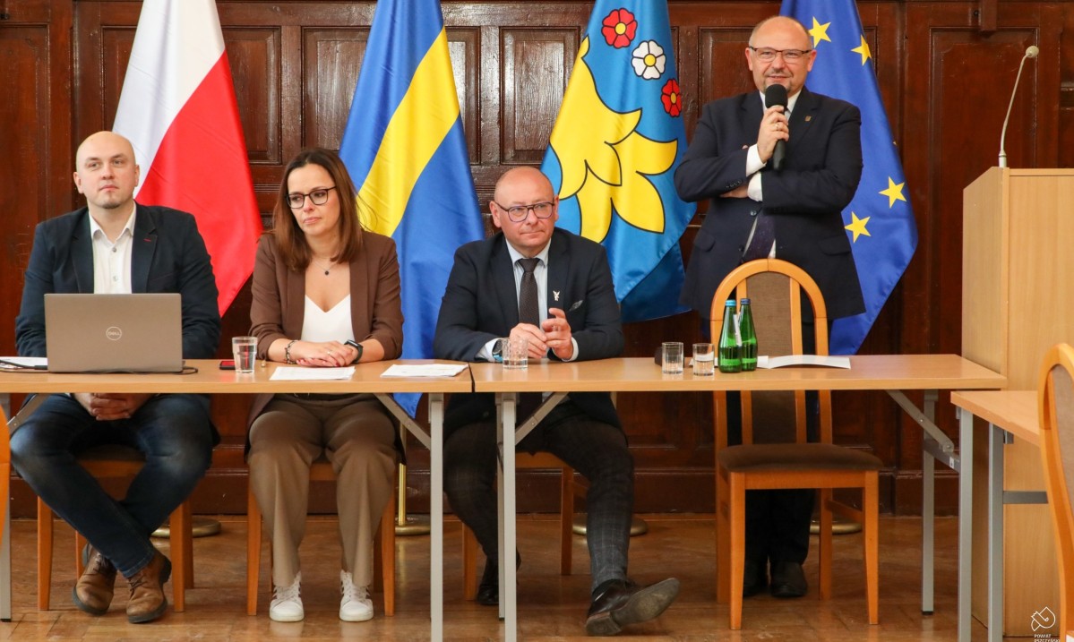 starosta mówi do mikrofonu, obok siedzi burmistrz oraz kobieta i męzczyzna.