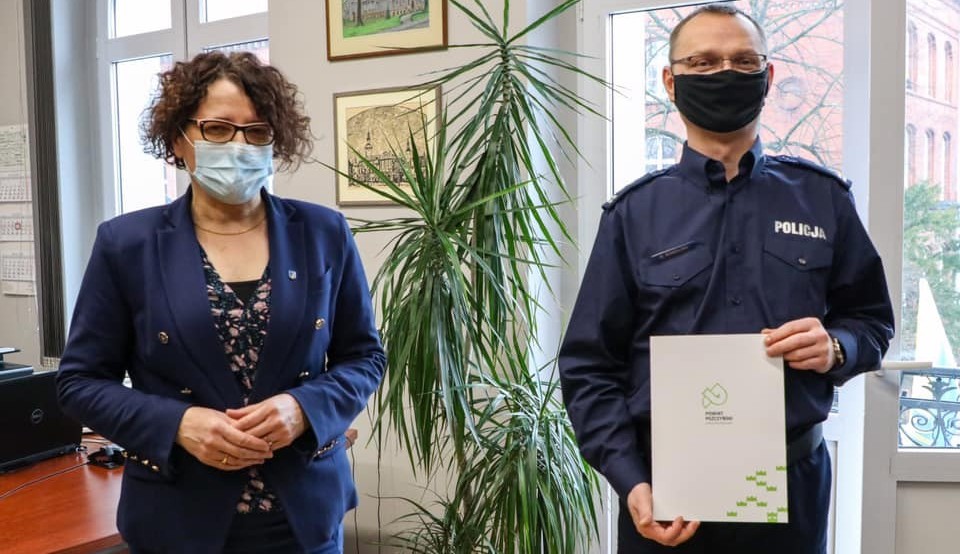 Kobieta i mężczyzna w mundurze policjanta stoją w jasnym pomieszczeniu.