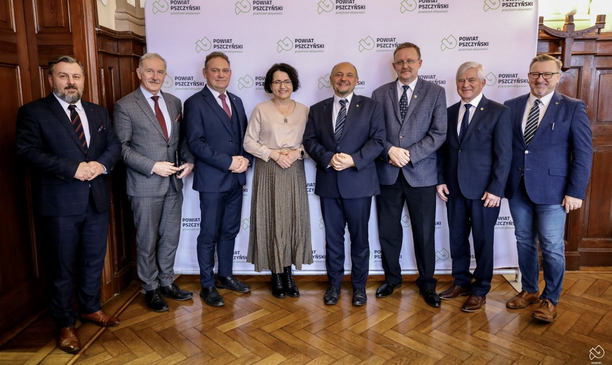 Członkowie zarządu powiatu i prezydium rady stoją na tle ścianki z logo powiatu