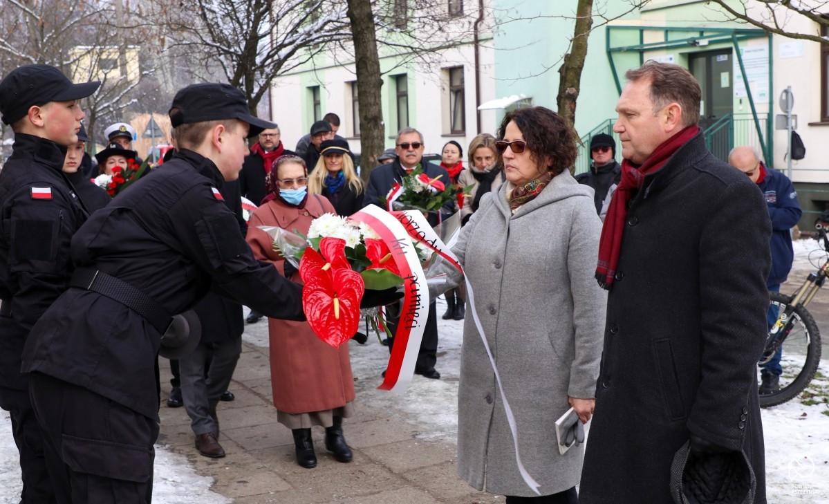 Starosta przekazująca wiązankę kwiatów na ręce ucznia klasy mundurowej. Obok niej wicestarosta.