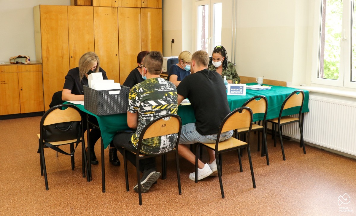 Młodzi mężczyźni w rejestracji do kwalifikacji wojskowej. Za stołem siedzą cztery kobiety rejestrujące.