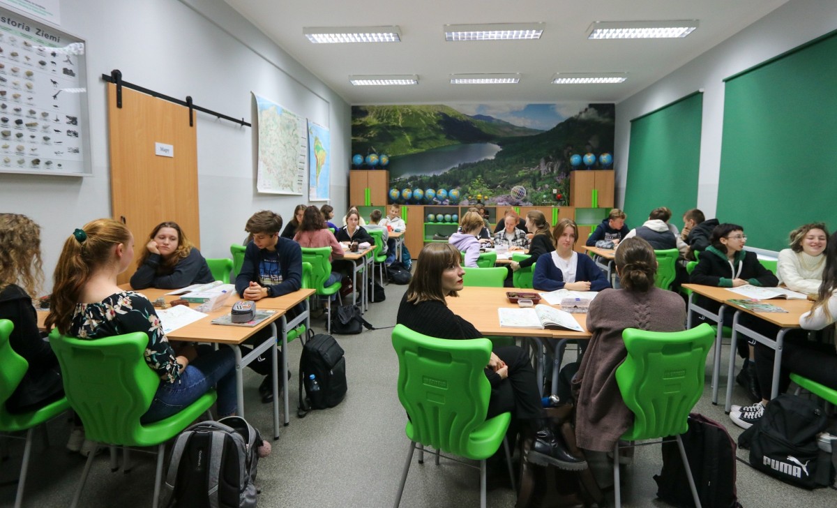 Nowoczesna zielona pracownia, w sali trwa lekcja. Za stołami siedzą uczniowie. Na ścianie fototapeta.