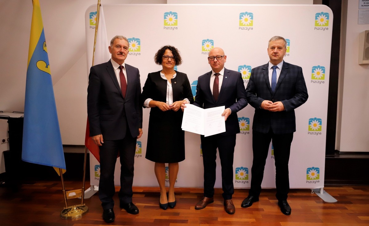 Na tle ścianki z napisem Pszczyna stoją Grzegorz Nogły, Barbara Bandoła, Dariusz Skrobol oraz Piotr Sidzina. Burmistrz trzyma dokumenty.