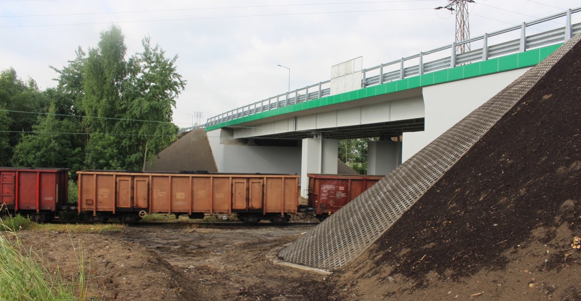 Przebudowany most w Suszcu. Betonowa konstrkcja, pod ktora prowadzą tory kolejowe. Przejeżdża pociąg towarowy.