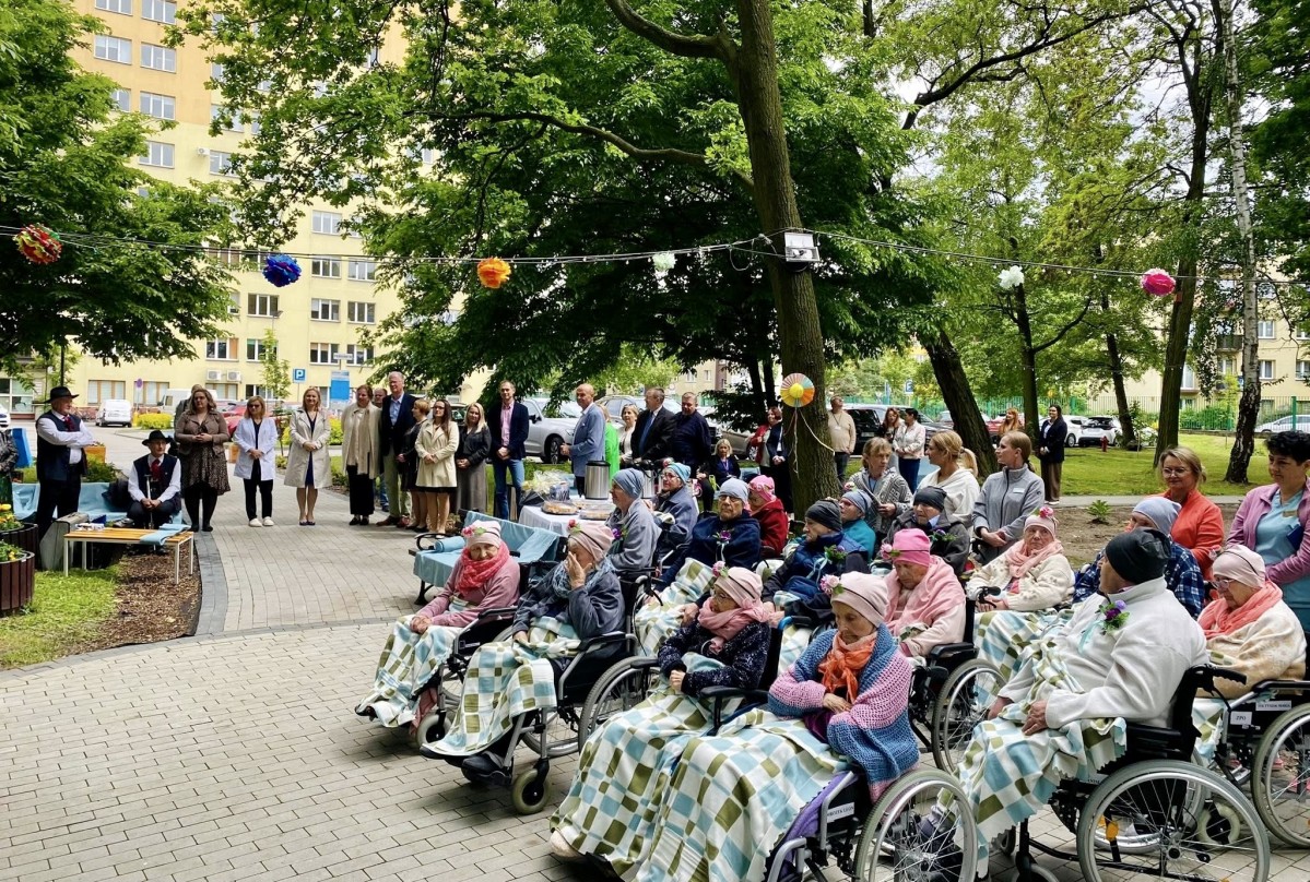 Seniorzy siedzący na wózkach w ogrodzie przy szpitalu.
