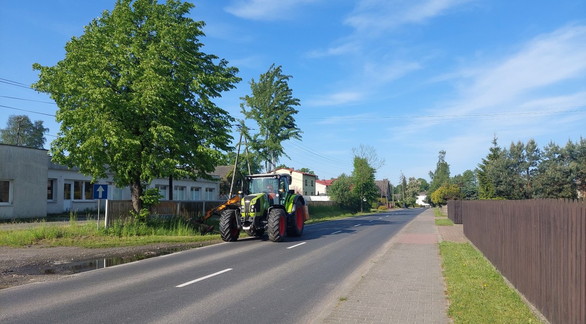 Zielony ciągnik wykonuje koszenie rowu za pomocą kosiarki wysięgnikowej