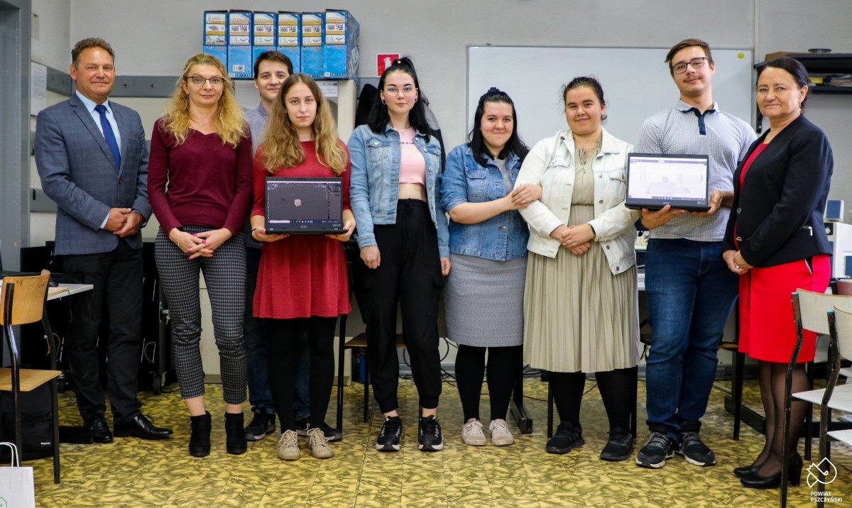 Uczniowie wraz z wicestarostą, dyrektor szkoły i koordynatorem projektu w sali komputerowej. Uczniowie trzymają w dłoniach laptopy.