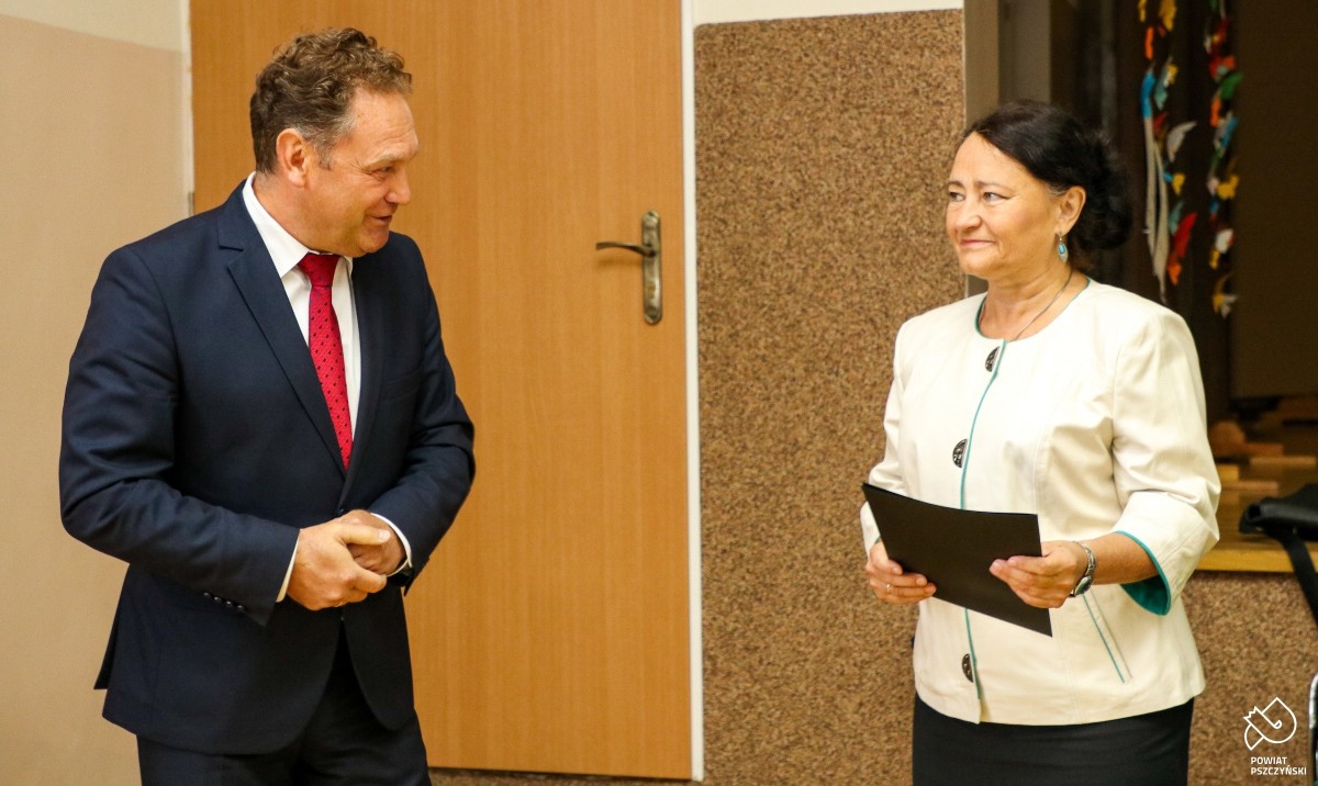 Wicestarosta Damian Cieszewski stojący obok dyrektor PZS nr 1 w Pszczynie, która w rękach trzyma dokument w czarnej teczce.