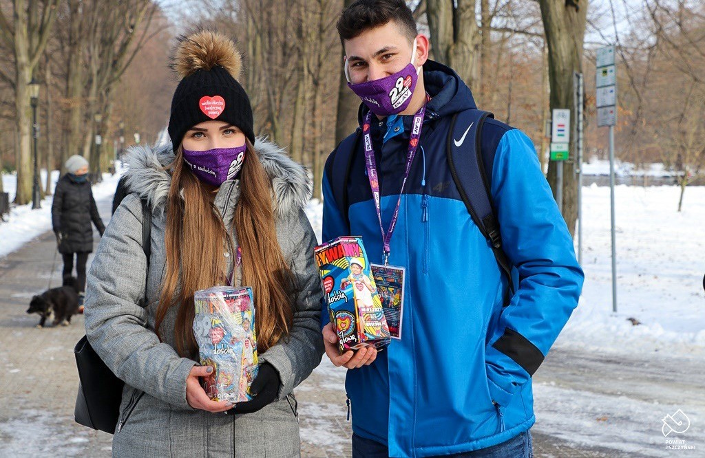 Dziewczyna z chłopakiem trzymają w dłoniach puszki WOŚP. Stoją na głównej alei w pszczyńskim parku.