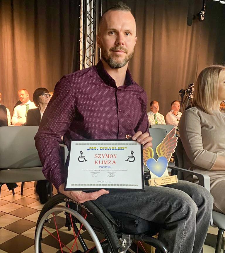 Mężczyzna na wózku inwalidzkim trzyma dyplom i statuetkę