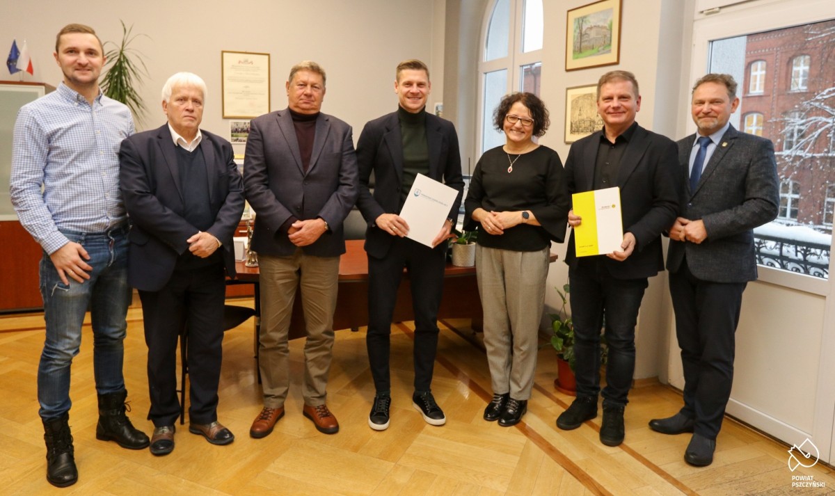 Uczestnicy spotkania, w tym Łukasz Piszczek i dyrektor szkoły, którzy trzymają w dłoniach porozumienia o współpracy.