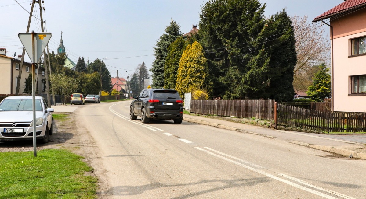 ul. Dworcowa w Piasku. Po drodze porusza się czarny samochód, na poboczu stoi srebrny samochód, przy drodze są zlokalizowane domy