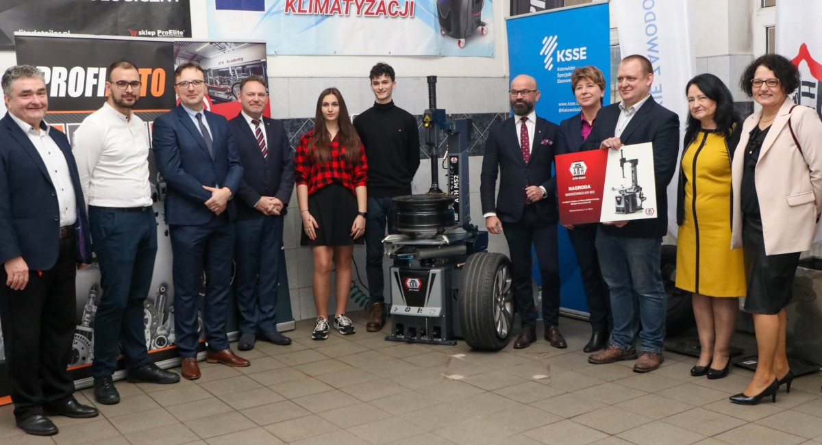 Osoby przekazujące montażownicę stoją obok urządzenia w pracowni motoryzacyjnej