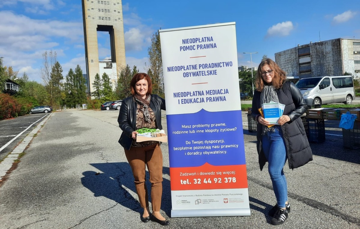 Kobiety stojące obok rollupa. W tle budynek szybu kopalnianego w Woli.
