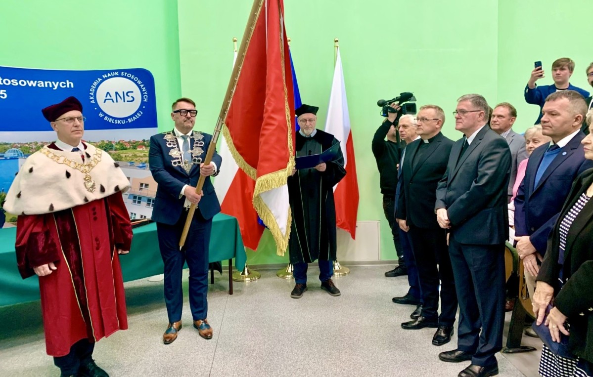 Prezydent Miasta trzyma sztandar, obok inne osoby, po prawej uczestnicy wydarzenia, w tym wicestarosta.