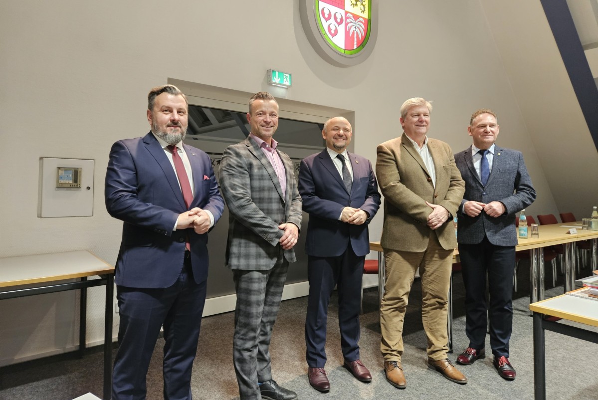 Starostowie i przewodniczący rad obu powiatów stoją, pozującv do wspólnego zdjęcia. Za nimi na ścianie widoczny herb powiatu anhalt-bitterfeld