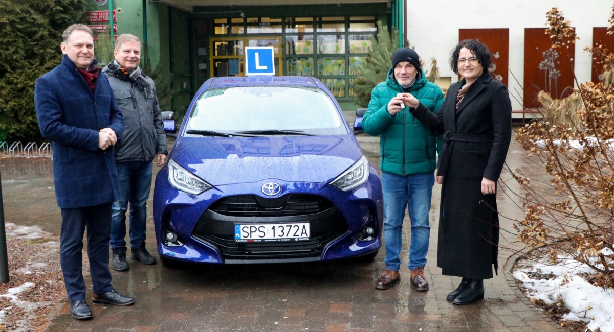 niebieski samochód obok któego stoją starosta, wicestarosta dyrektor i nauczyciel