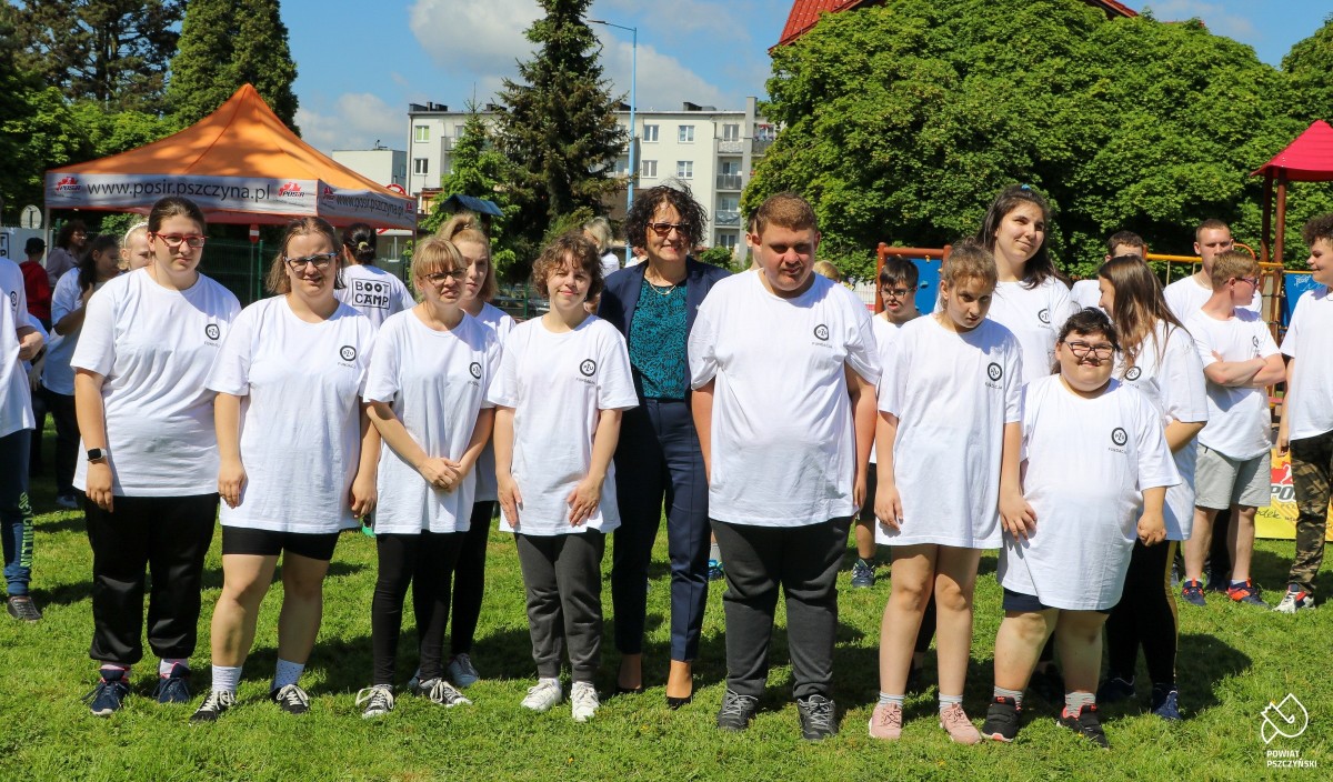 Osoby z niepełnosprawnościami w białych koszulkach wraz z nimi stoi starosta na boisku. Uśmiechają się.